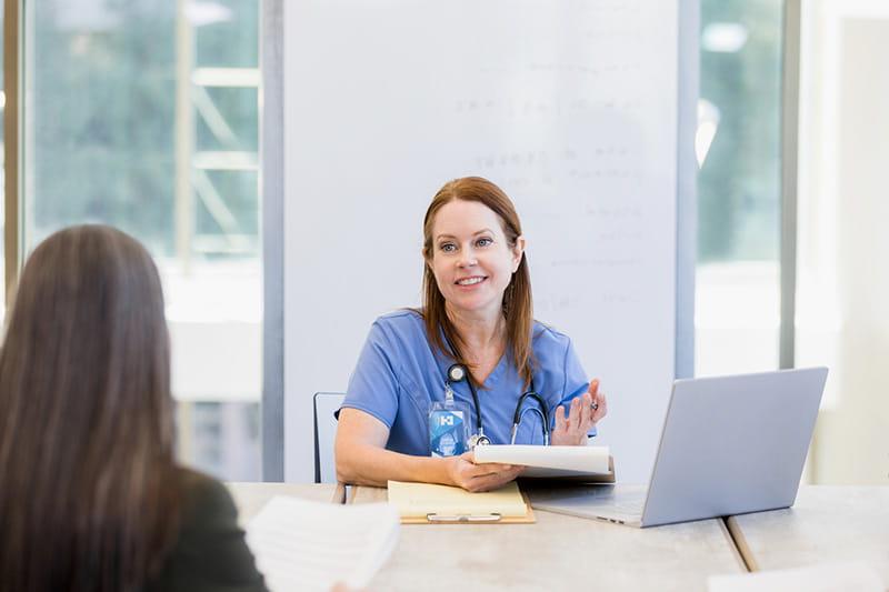 医疗保健专业人员坐在笔记本电脑前拿着剪贴板，对同事微笑
